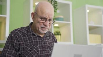 antiguo hombre utilizando ordenador portátil a hogar y consiguiendo frustrado. antiguo hombre recepción malo y angustioso Noticias en ordenador portátil. video