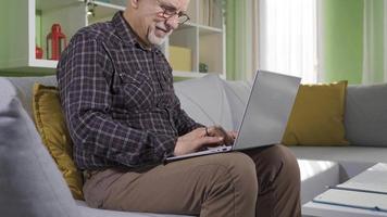 oud Mens Bij huis gebruik makend van laptop en lachend, hebben pret en vrolijk. oud Mens zittend Aan sofa Bij huis gebruik makend van laptop pret en gelukkig. video