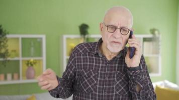 frustriert alt Mann reden auf das Telefon ist beim heim. das alt Mann reden auf das Telefon im Vorderseite von das Kamera beim Zuhause bekommt wütend, Verwendet Wörter er nicht wollen, und Anrufe Betrüger. video