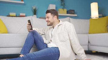 content Jeune homme souriant et à la recherche à le téléphone. Jeune mignonne content homme dépenses temps sur téléphone à maison. video