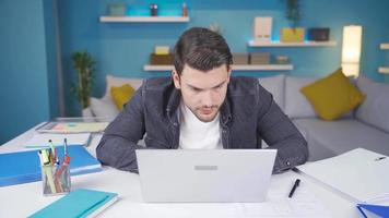 jovem homem trabalhando a partir de computador portátil piscando olhando às Câmera. jovem homem trabalho a partir de computador portátil e levanta dele cabeça para a Câmera e piscadelas. video