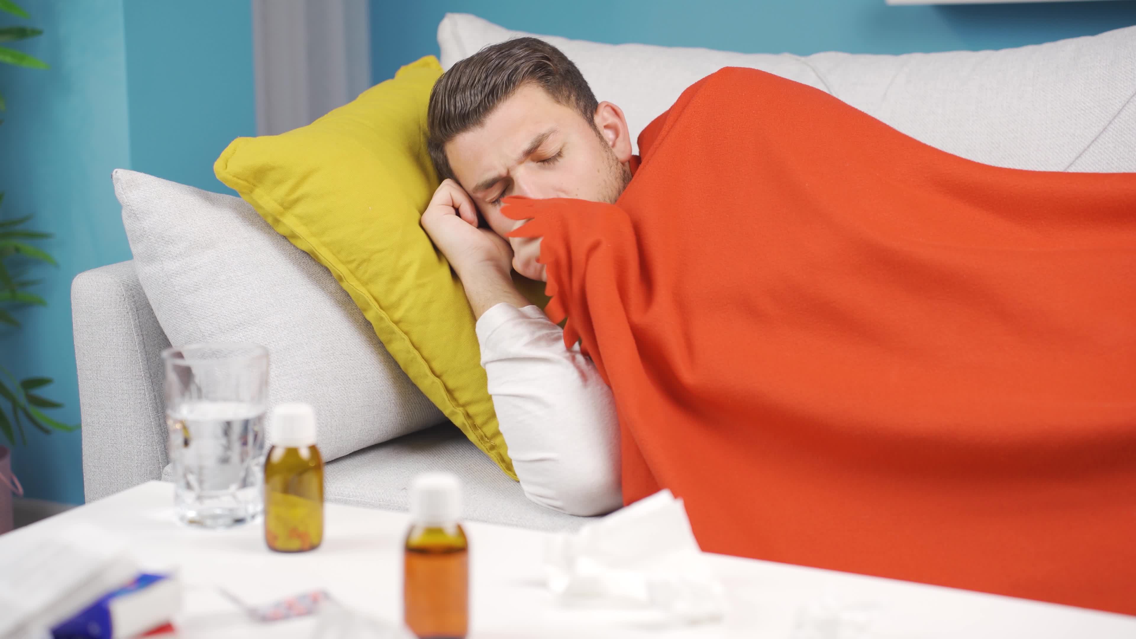 Sick man lying on sofa and drinking water in pain. The sick young man