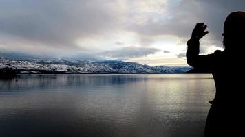 woman waving to snow mountain by the lake on a cloudy day video