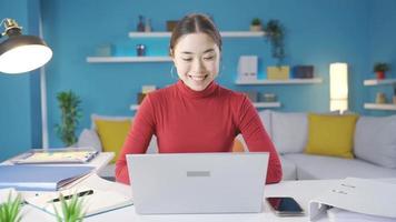 Asian woman working in home office working from laptop in happy and moody mood. Young Asian woman working on laptop rejoices, feels happy, in good spirits when things go well. video