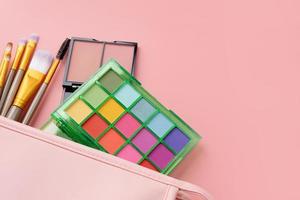 Bright summer eyeshadow palette and makeup products in pink cosmetic bag on pink background photo