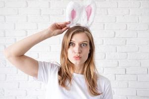 Portrait of a happy woman in bunny ears on white brick wall background photo