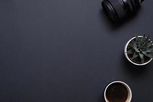 Photographer work desk composition with camera lens, plant and coffe mug. Top view, flat lay with copy space on black desk photo