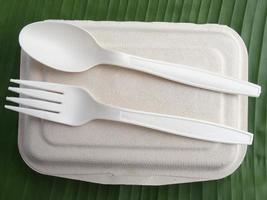 Bio Plastic spoon and fork on natural fiber lunch box on green banana leaf photo