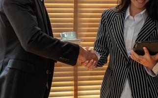 Businessman and businesswoman shaking hands while standing in front of window blind in office. Business meetings concept photo