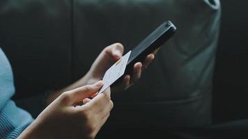 Close up smiling millennial woman holding smartphone and banking credit card, involved in online mobile shopping at home, happy female shopper purchasing goods or services in internet store. video