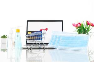 Credit card in shopping cart front of laptop screen with surgical mask
