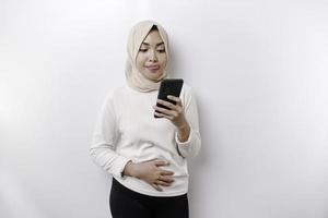 A thoughtful young Asian Muslim woman wearing a hijab and holding her chin while talking on the phone isolated by a white background photo