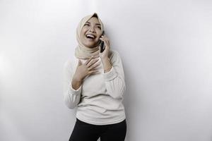 A happy Asian Muslim woman wearing a headscarf, holding her phone, isolated by white background photo