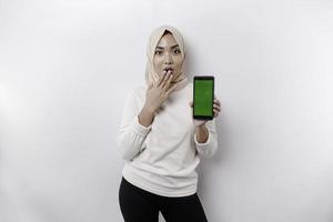 conmocionado asiático mujer vistiendo Pañuelo, demostración Copiar espacio en su teléfono pantalla, aislado por blanco antecedentes foto