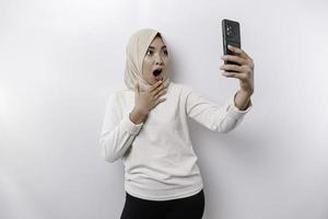 conmocionado asiático mujer vistiendo Pañuelo, participación su teléfono, aislado por blanco antecedentes foto