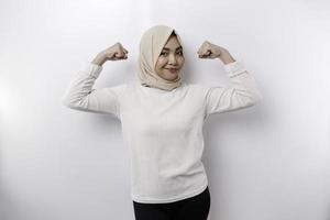 Excited Asian Muslim woman wearing a headscarf showing strong gesture by lifting her arms and muscles smiling proudly photo