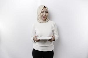 An Asian Muslim woman is fasting and hungry and holding a plate while looking aside thinking about what to eat photo