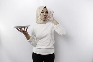 A smiling Asian Muslim woman is fasting and hungry and holding and pointing to a plate photo