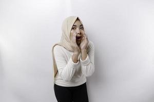 Young beautiful Asian Muslim woman wearing a headscarf shouting and screaming loud with a hand on her mouth. communication concept. photo