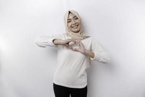 A happy young Asian woman wearing headscarf feels romantic shapes heart gesture expresses tender feelings photo