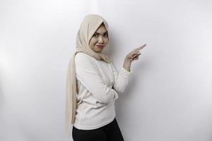 A thoughtful young Asian Muslim woman is wearing hijab and looks confused between choices, isolated by a white background photo