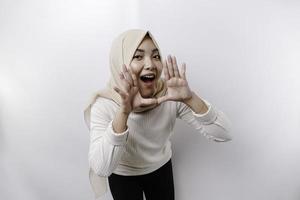 joven hermosa asiático musulmán mujer vistiendo un Pañuelo gritos y gritando ruidoso con un mano en su boca. comunicación concepto. foto