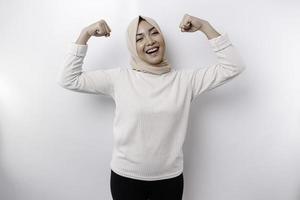 emocionado asiático musulmán mujer vistiendo un Pañuelo demostración fuerte gesto por levantamiento su brazos y músculos sonriente con orgullo
