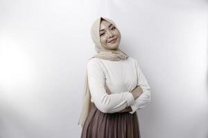 A confident smiling Asian Muslim woman wearing hijab standing with arms folded and looking at the camera isolated over white background photo