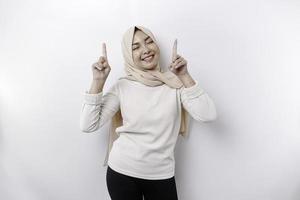 emocionado asiático musulmán mujer vistiendo hijab señalando a el Copiar espacio encima su, aislado por blanco antecedentes foto
