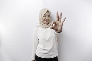 A smiling Asian Muslim woman, giving an OK hand gesture isolated over white background photo