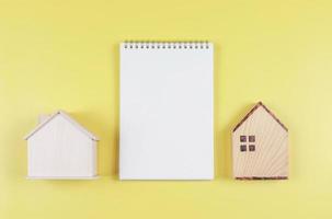 flat layout of  blank page notebook  and two wooden model houses  on yellow  background with copy space, home purchase planning  concept. photo