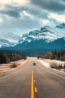 Road trip on highway between pine forest driving straight to rocky mountains in Icefields Parkway photo