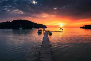 Beautiful sunset over tropical sea and wooden pier, sightseeing boat and tourist enjoying in Koh Kood Island photo