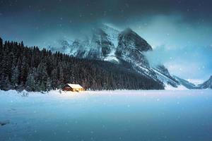 Scenery of Lake Louise with wooden cottage glowing and rocky mountains with snow covered in winter at Banff national park photo