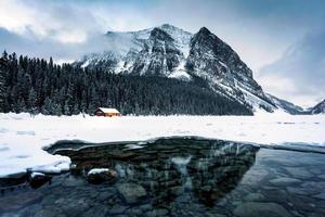 Scenery of Lake Louise with wooden cottage glowing and rocky mountains with snow covered in winter at Banff national park photo