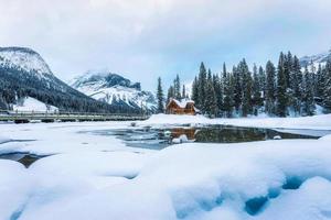 Frozen Emerald Lake with wooden lodge in pine forest on winter photo