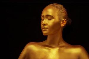 modelo niña con dorado profesional Arte maquillaje en un negro antecedentes. hermosa dorado metálico cuerpo, labios y piel foto