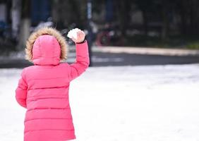 linda niña Listo a lanzar bola de nieve durante día, perspectiva desde detrás foto