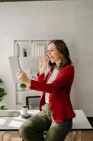 Working woman concept a female manager attending video conference and holding tablet, smatrphone and  cup of coffee in office photo