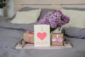 A bouquet of lilacs and a card with the text I love mom on a tray. Mother's day concept photo