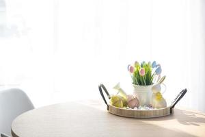 Easter decoration of colorful eggs, fresh grass in a watering can, easter bunny on a tray on the round table in a rustic style. Festive interior of a country house photo