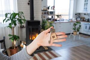 llave de casa con llavero contra el fondo de la estufa de chimenea con fuego y leña. acogedor hogar hogareño. construcción, diseño, proyecto, mudanza a casa nueva, hipoteca, alquiler y compra de bienes raíces foto