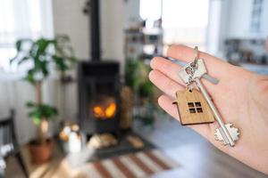 Key to house with keychain against background of fireplace stove with fire and firewood. Cozy home hearth. Building, design, project, moving to new house, mortgage, rent and purchase real estate photo