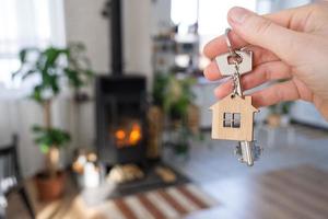 Key to house with keychain against background of fireplace stove with fire and firewood. Cozy home hearth. Building, design, project, moving to new house, mortgage, rent and purchase real estate photo