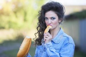 Funny young woman in a denim jacket with make-up in the style of the eighties eats a loaf. photo