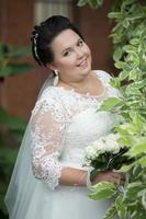 Vertical portrait of a dark-haired fat bride with a wedding bouquet. photo