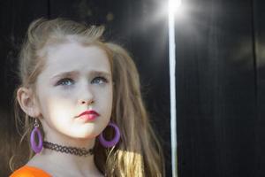 Portrait of a little girl with bright makeup standing by a wooden fence. Red-haired little girl. photo