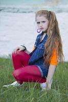 retrato de un pequeño Pelirrojo niña con brillante maquillaje en un mezclilla chaleco y rojo polainas. foto