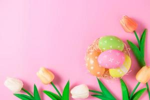 Happy Easter holiday greeting card concept. Colorful Easter Eggs and spring flowers on pastel pink background. Flat lay, top view, copy space. photo