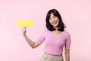 Portrait happy young woman model holding and showing blank space paper for advertisement information message poster with thumb up or point finger gesture isolated on pink pastel studio background. photo